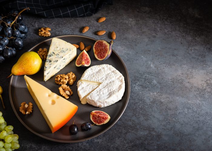 Cheese plate. Assortment of cheese with nuts and fruits on wood serving board over gray concrete texture background. Top view with copy space. Appetizer theme, keto diet. Copy space