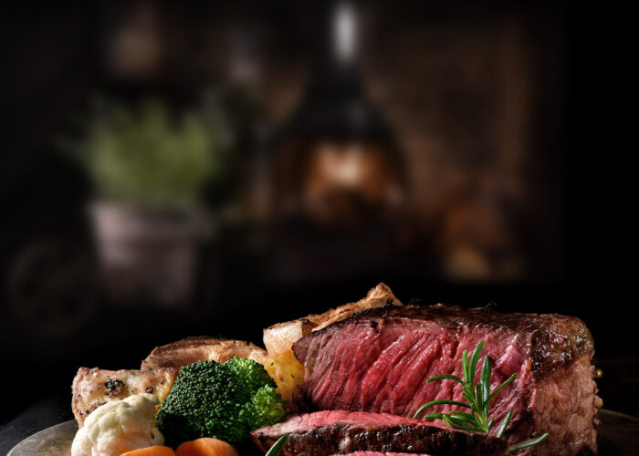 Succulent side of rare roast beef with seasonal vegetables, Yorkshire Puddings and roast potatoes with Rosemary garnish shot in a rustic setting with an old fashioned wood burner. Copy space.